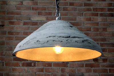 Artisan concrete pendant light showing chain hook and concrete surface detail, and inner area of the shade with the bulb lit